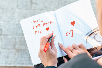 Young Woman lefty writes in a notebook. holds felt-tip pen in her left hand.Outdoors summer evening park. Left-handers Day August 13th.Closeup.