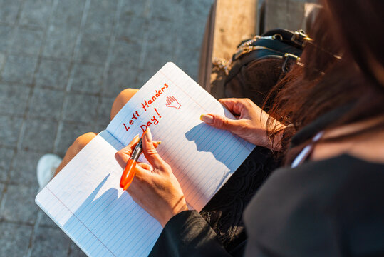 Left-handers Day.Woman writes in a notebook, holds felt-tip pen in her left hand.Outdoors summer evening park.August 13th.Closeup.
