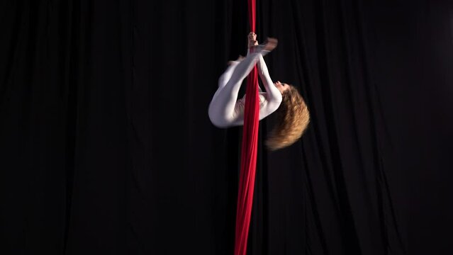 Professional circus performer. A flexible girl performs on stage on red aerial silks. Graceful curly-haired gymnast performs splits and gymnastic elements while dancing on canvases
