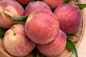 Fresh Peach fruits with leaves on bamboo basket, Korean white peach in Bamboo basket on wooden table.