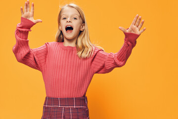 a beautiful, sweet girl in bright, pink clothes, stands on a yellow background with her hands raised high. Horizontal studio photo with empty space to insert advertising layout