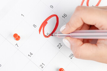 female hand marking with a red pen on a 15th day of the month  calendar circles the day, deadline concept