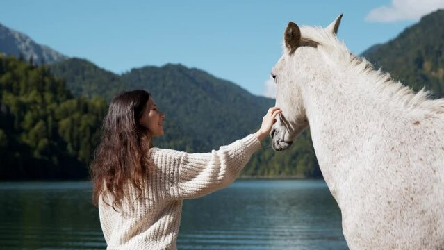 Mysterious asian woman tourist with animal horses wild white sunset running rider cowboy water Amazing view turquoise water high mountain lake Braies mountains. Casual boho style clothing back view