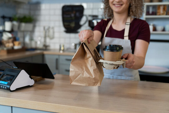 Young caucasian waitress selling take away food in disposable package