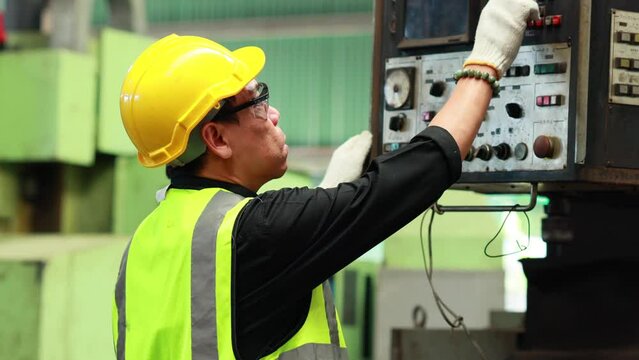 Metal machine in heavy Industry Manufacturing. Asian male factory worker wearing safety hard hat helmet control lathe machine to drill components.