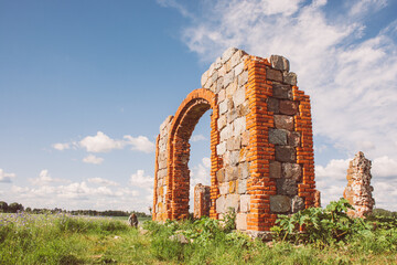 An old, dilapidated stone and brick building in a meadow under a dramatically cloudy sky. Old rural property.