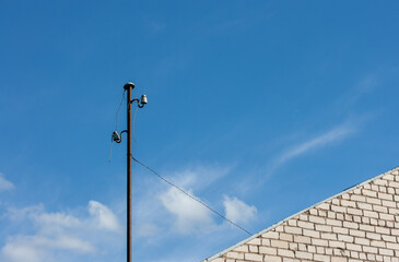 An old electric metal pole with wires at the corner of the house on a sunny summer day with a blue...
