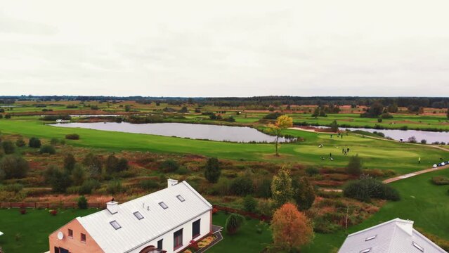 Aerial outdoor view of a beautiful calm rich landscape with big modern houses, people playing golf and clear small ponds. High quality 4k footage