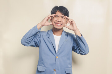 young asian man wearing college suit having headache on isolated background
