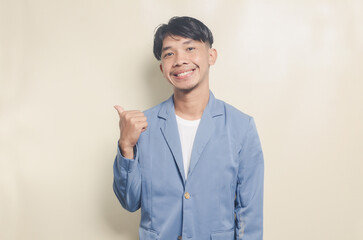 young asian man wearing college suit pointing to empty space on isolated background