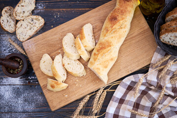Fresh baguette and sliced bread on wooden cutting board at kitchen table