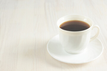 A cup of invigorating black coffee on a light wooden background. Selective focus, toned image, natural light. copy space for text