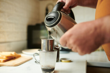 Fototapeta na wymiar Closeup image of man pouring hot water in phin filter when making cup of coffee at home