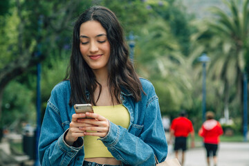 smiling young girl shopping in the park with bags and mobile phone