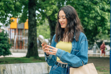 smiling young girl shopping in the park with bags and mobile phone