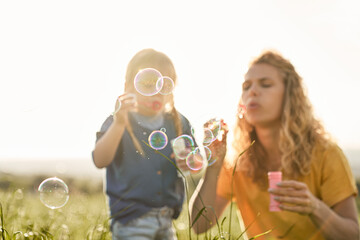 Caucasian mom with daughter blowing bubble at the meadow