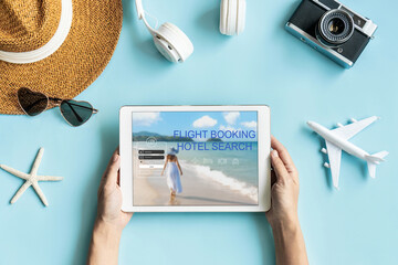 Flat lay of hands holding tablet and travel accessories on blue color background. Travel, summer vacation concept. Copy space for text, top view