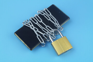Privacy and security concept. Chained smartphone with padlock on blue background close-up. 