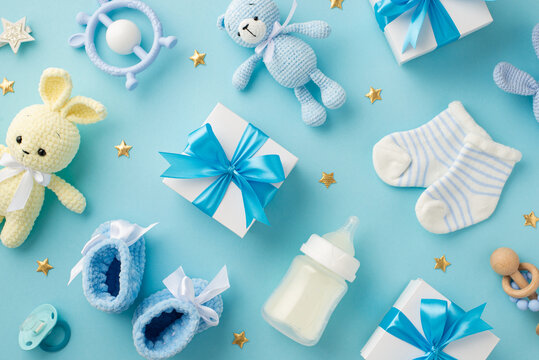 Baby accessories concept. Top view photo of gift boxes teether knitted bunny and teddy-bear toys socks shoes milk bottle rattle pacifier and gold stars on isolated pastel blue background