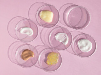 Multicolored textures of cream, scrub, serum and gel in Petri dishes on a pink background. Concept of cosmetics laboratory researches. Smear of skincare cosmetics product. Wellness and beauty concept