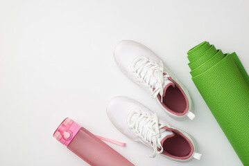 Sports accessories concept. Top view photo of white sneakers pink bottle of water and green yoga...