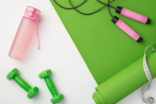 Fitness accessories concept. Top view photo of pink bottle of water green sports mat dumbbells skipping rope and tape measure on isolated white background
