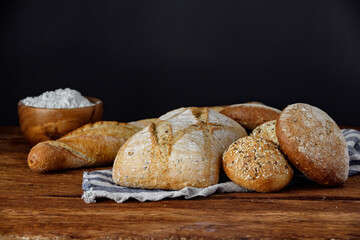 Assorted different types of bread on a wooden table on a black background.