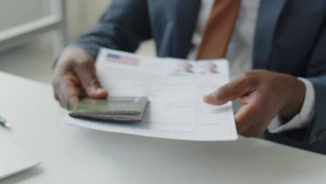 Close up tilt up shot of African American visa officer taking documents and passport form applicant and asking questions during interview in U.S. embassy