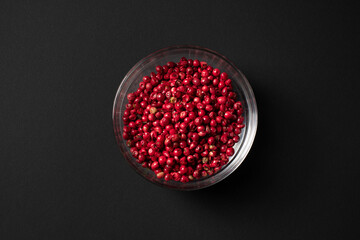 pink peppercorns in glass bowl isolated on black background