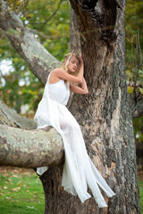 Beautiful blonde woman in a white dress sitting on a tree