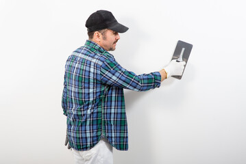 Male builder in a cap plastering a white wall