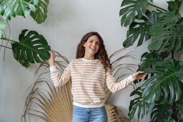 Portrait of happy positive young German woman among Monstera leaves at cozy tropical home garden, smiling optimistic Hispanic female gardener at urban jungle apartment. Gardening, hobby concept