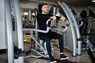 Fototapeta na wymiar Muscular arab man training and doing workout on fitness machine in modern gym.