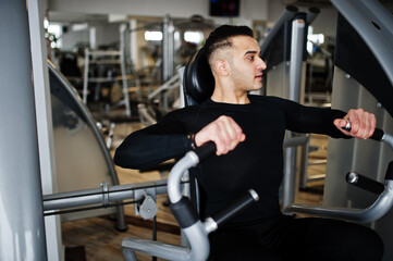 Muscular arab man training and doing workout on fitness machine in modern gym.