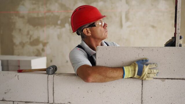 Bricklayer or mason lays bricks to construct wall of autoclaved aerated concrete blocks. Brickwork worker contractor constructs blockwork with foam concrete doing precise masonry with a laser level.