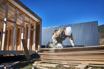 Carpenter using circular saw for cutting wooden OSB board. Man worker building wooden frame house on pile foundation. Carpentry concept.