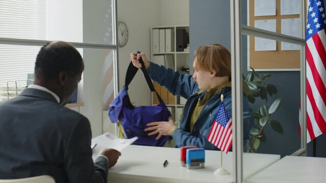 Young Caucasian man walking in U.S. embassy, giving documents to African American consulate officer and answering his questions during visa interview