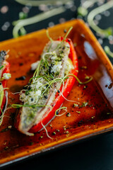 stuffed peppers, bell peppers with meat on a plate with sprouts of herbs, on a black table