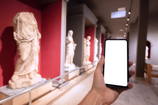Smartphone with a blank screen in the interior of an archaeological museum with antique greek statues. Concept of an audio guide and e-learning mobile application