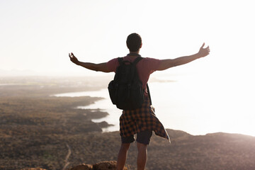 Young man standing on the stone with raised up arms. Tourist man on the top of the mountain