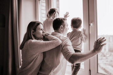 black and white portrait of caucasian family looking out the window. Little boy and girl standing on sill. Staying home during pandemia. Image with selective focu