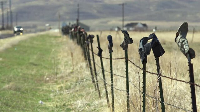 Fence on side of country road with old boots on the top of each post as car is driving Malad, Idaho.