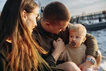 Family. mom, dad and baby boy sitting at the quay, parents looking at son sucking a dummy. image...