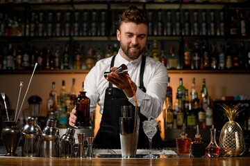 various shakers and bottles stand on the bar counter and male bartender accurate pours alcoholic...