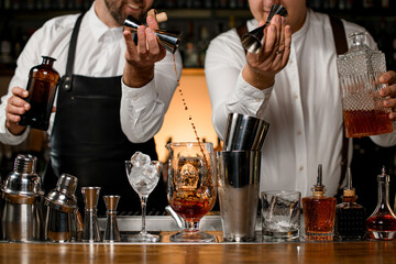 great view on mixing cup with ice and shaker cups on the bar counter into which the bartenders masterfully pouring the drinks