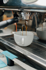 Pouring coffee flow from a professional machine into a cup. The barista makes a double espresso using a filter holder. Flowing fresh ground coffee. Drinking roasted black coffee in the morning