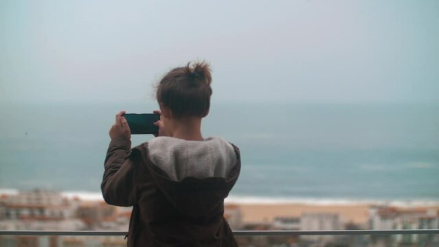 Child taking scenic shots of ocean coast in Nazare, Portugal