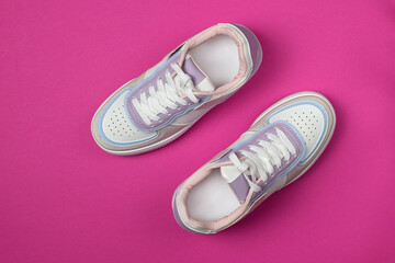 New white sneakers on a bright pink background. Trendy colorful photo in minimal style. Top view, flat lay.