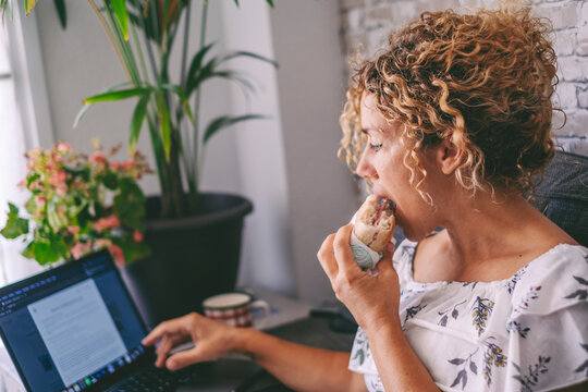 One woman working on laptop and eating a sandwich for lunch break time. Modern people work on computer at home. Alternative office and digital online job concept. Fast food nutrition concept lifestyle