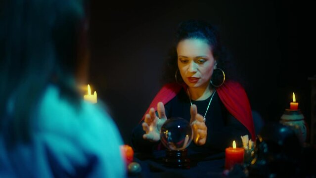Professional witch working with crystal ball, telling fortune to female client